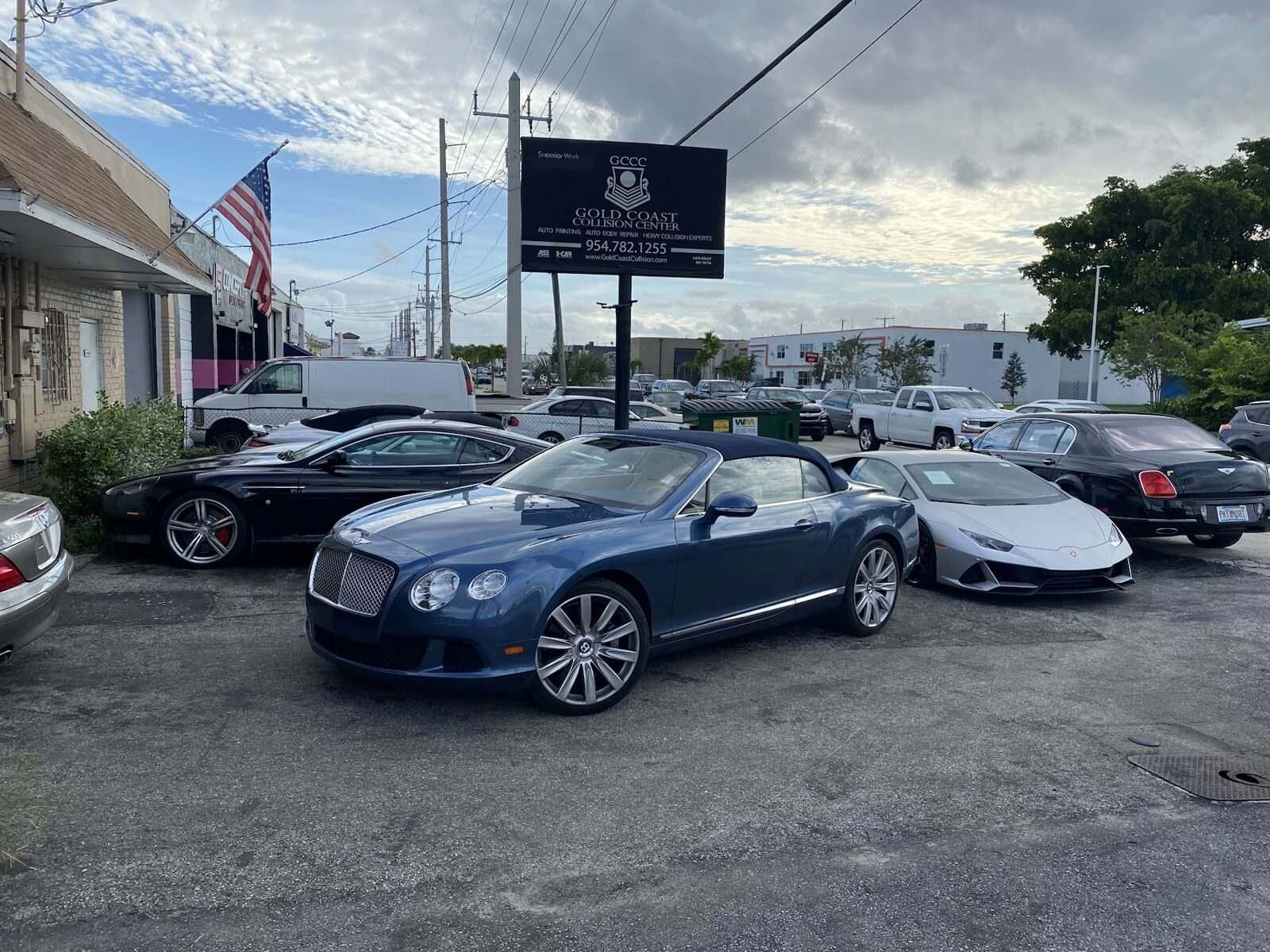 Gold Coast Collision Center sign with a Bentley and a Lamborghini Huracán in front of the shop
